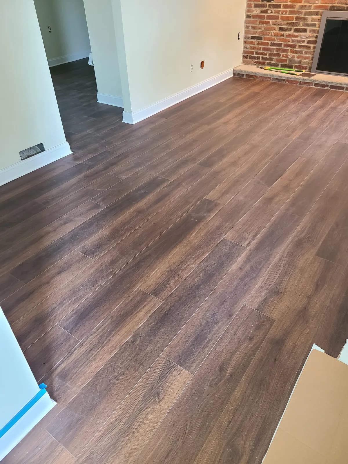 Warm brown wood-look LVP flooring by a brick fireplace — installed by Threshing Floors