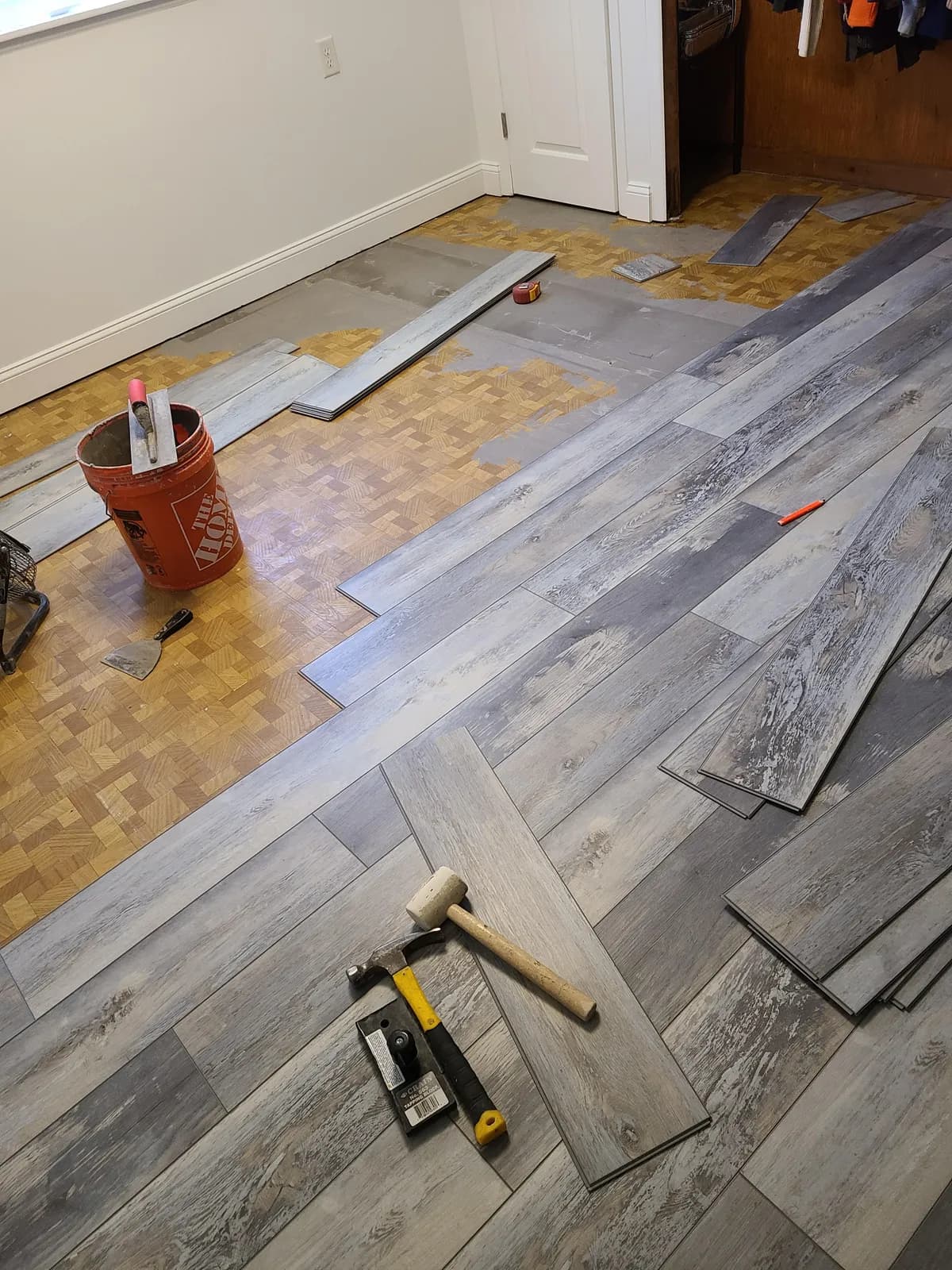 New gray LVP planks being installed directly over an existing parquet floor with installation tools