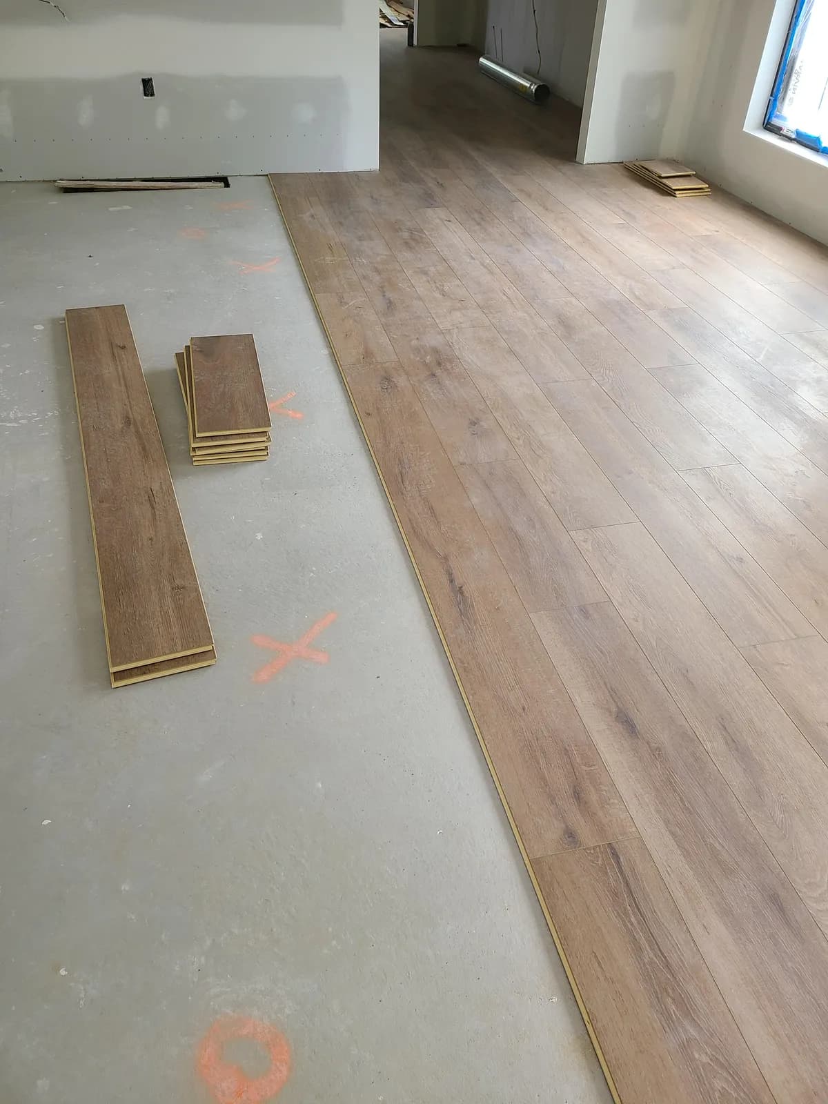 Chalk layout lines on a concrete subfloor with LVP planks staged for a straight install